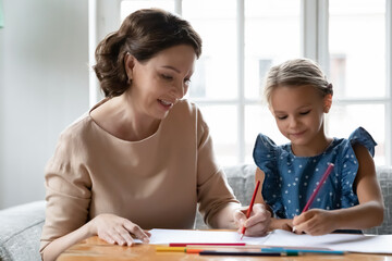 Close up smiling mature grandmother and granddaughter drawing colored pencils together, sitting at...