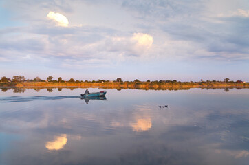 Fototapeta na wymiar Boat and ducks on calm morning river, simmetrical reflection of purple clouds. River Samara.