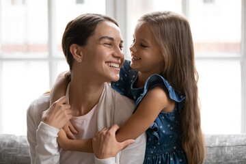 Close up smiling little girl hugging young beautiful mother, enjoying tender moment, happy mum and...