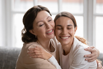 Close up head shot happy middle aged mother and grownup daughter cuddling, hugging, excited by good news, feeling gratitude, smiling young woman with mature mum enjoying tender moment at home