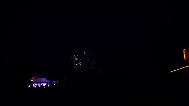 Real fireworks at night in an open natural area with an illuminated tent and a house