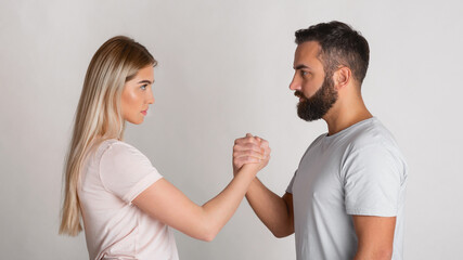 Young guy and girl look at each other seriously and squeeze their hands in arm wrestling