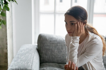 Obraz premium Close up upset thoughtful young woman looking to aside, thinking about relationship personal problems, pensive frustrated female lost in thoughts, sitting on couch at home alone, feeling depressed