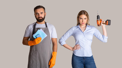 Gender stereotypes and non female profession. Serious man in apron and rubber gloves holding sponges and woman holding a drill - obrazy, fototapety, plakaty