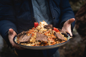 a man holds a plate of pilaf in his hands. traditional Uzbek dish. rice with vegetables and meat