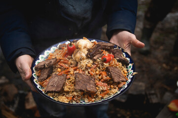 a man holds a plate of pilaf in his hands. traditional Uzbek dish. rice with vegetables and meat