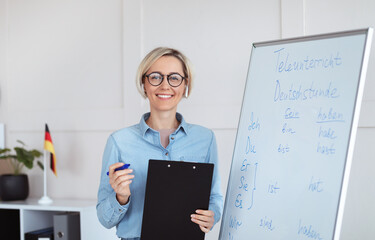 Online schooling. Positive German teacher posing near blackboard with grammar rules, looking at...