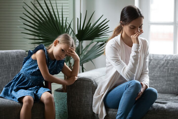 Fototapeta na wymiar Upset mother and little daughter ignoring each other, family generations conflict concept, misunderstanding, frustrated mum and girl child avoiding talk after quarrel, sitting on couch at home