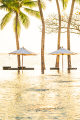 Beautiful landscape of swimming pool with umbrella and chair nearly sea beach ocean at sunrise sunset time