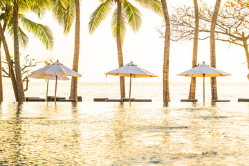 Beautiful landscape of swimming pool with umbrella and chair nearly sea beach ocean at sunrise sunset time