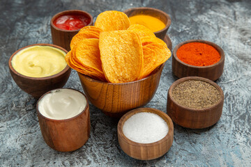 Close up view of crispy chips on wooden cutting board and different spices on gray table