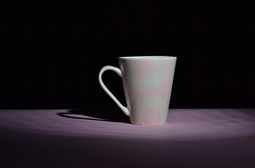 pink ceramic cup in the darkness on pink desk and isolated on black background, copy space
