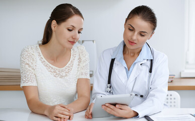 Doctor and patient are sitting and discussing health examination results while using tablet computer. Health care, medicine and good news concepts