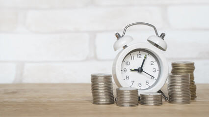 white analog clock and blurred stack of coins on wooden desk for finance and business concept ,...