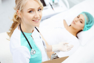 Female doctor and young woman patient in hospital. Physicians examine girl lying at the bed, view from above