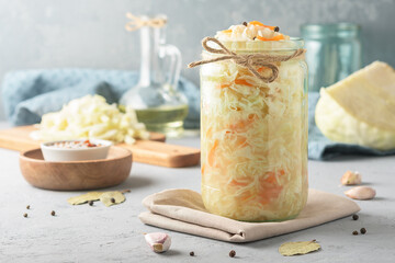 Sauerkraut in a glass jar with ingredients on a concrete background. - obrazy, fototapety, plakaty