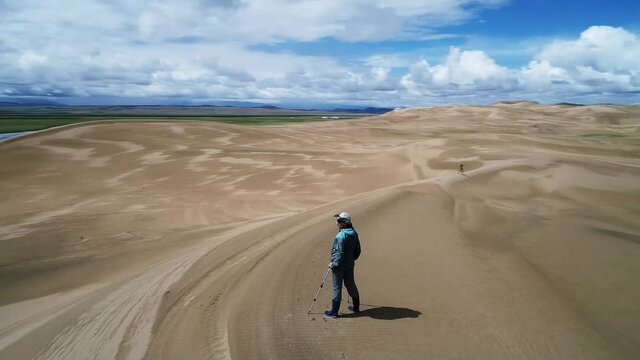 Tourist standing at the top of the sand dune. Large barkhan in Mongolia sandy dune desert Mongol Els. Govi-Altay, Mongolia.  Aerial View, Point of interest