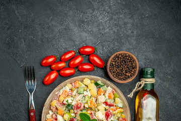 top close view of bowl of veggie salad with fork tomatoes pepper and oil on side and free place for text on dark grey table