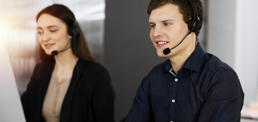 Call center operators at work. Two young people in headsets are talking to the clients, while sitting in sunny office
