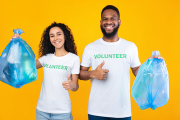 Couple Of Volunteers Holding Plastic Garbage Bags Over Yellow Background