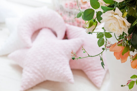 Gentle pink background with soft pillows near the window and roses in interior. 