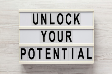 'Unlock your potential' on a lightbox on a white wooden surface, top view. Flat lay, overhead, from above.