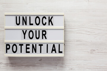 'Unlock your potential' on a lightbox on a white wooden background, top view. Flat lay, overhead, from above.