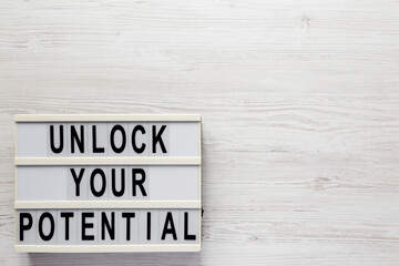 'Unlock your potential' on a lightbox on a white wooden surface, top view. Flat lay, overhead, from above.