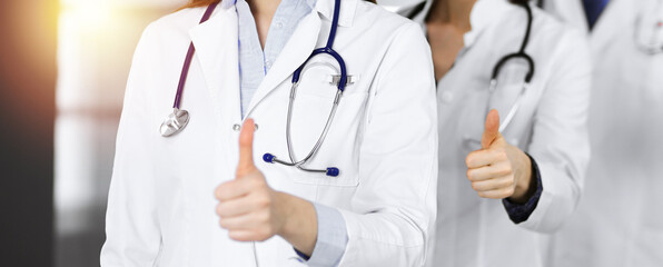 Group of doctors standing as a team with thumbs up in sunny clinic. Good news and Hope for a cure. Medicine concept during Coronavirus pandemic. Covid-2019