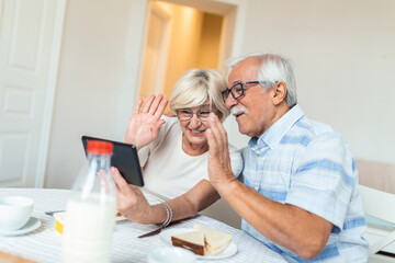 Fototapeta premium Senior man and his wife are using a digital tablet and communicating with their kids. Happy senior couple is having breakfast and having an online conversation with their family and sending greetings.