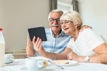 Senior couple smiling and looking at the same tablet hugged. Indoor, at home concept. Mature and retired man and woman using technology - lockdown and quarantine lifestyle