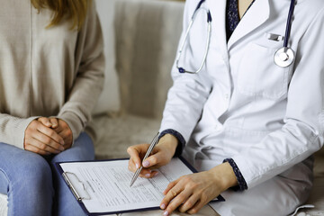 Unknown woman-doctor and patient discussing current health examination while sitting indoors. Stay...