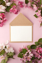 Floral springtime composition with pink apple tree flowers and craftpaper envelope, white blank card for you text, mock up on pink background. Flat lay. Top view.