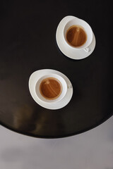 Defocused Two white coffee cups on a table with blurred balcony partition light background. Selective focus. Flat lay