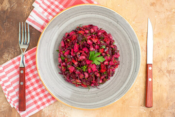 top close view of plate of a red salad in the center with greens on it with cutleries at both sides and checked napkin at the side on a wooden backgorund