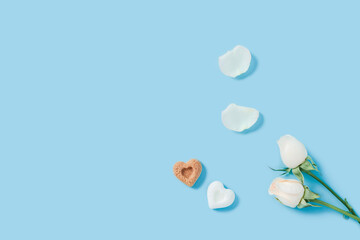 Holiday card on a blue background. Romantic photo with roses and petals and two pieces of sugar in the form of hearts. Happy morning.