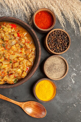 top view roasted eggplant salad in bowl different spices in small bowls a wooden spoon on dark background
