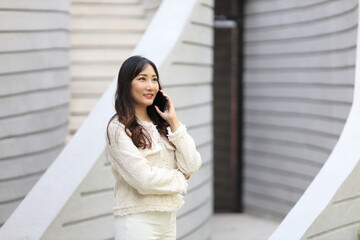 Fototapeta premium Asian lady using mobile phone while walking along the modern building in urban downtown area for communication and technology concept