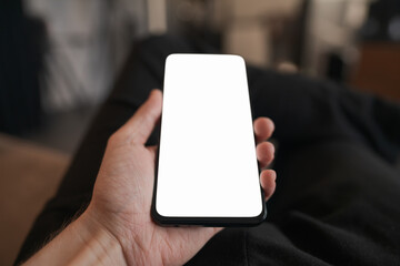 Man hold smartphone with white screen in his hand sitting on a couch in home environment