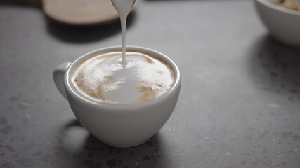 Pour steamed milk into espresso to make cappuccino on concrete countertop closeup