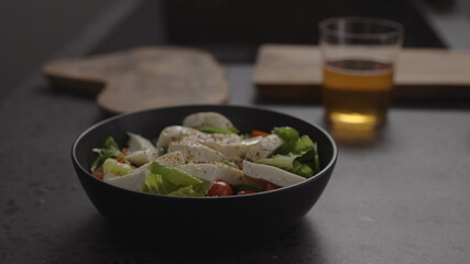 salad with mozzarella and tomatoes in black bowl and apple cider in glass on concrete countertop