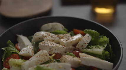 salad with mozzarella and tomatoes in black bowl and apple cider in glass on concrete countertop