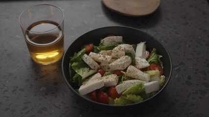 salad with mozzarella and tomatoes in black bowl and apple cider in glass on concrete countertop