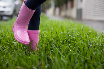 Young girl child wearing pink gumboots on the grass outdoors on rainy day