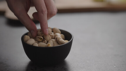 man hand take pistachio from black bowl on terrazzo surface
