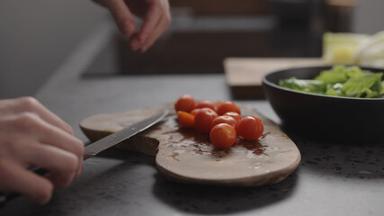 man hand cutting cherry tomatoes into halves on wood board on home kitchen