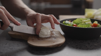 man hands slicing mozzarella on wood board on home kitchen