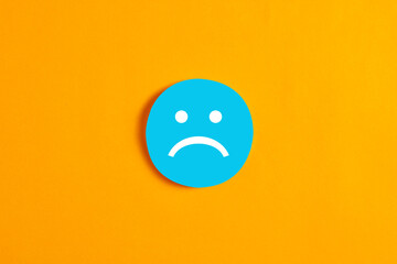 Blue round circle with a sad face icon against yellow background. - obrazy, fototapety, plakaty