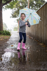 Young girl child holding umbrella at walking along the street during rain