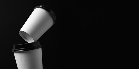 White paper coffee cups with black lid on black background with copy space. Mockup for branding.